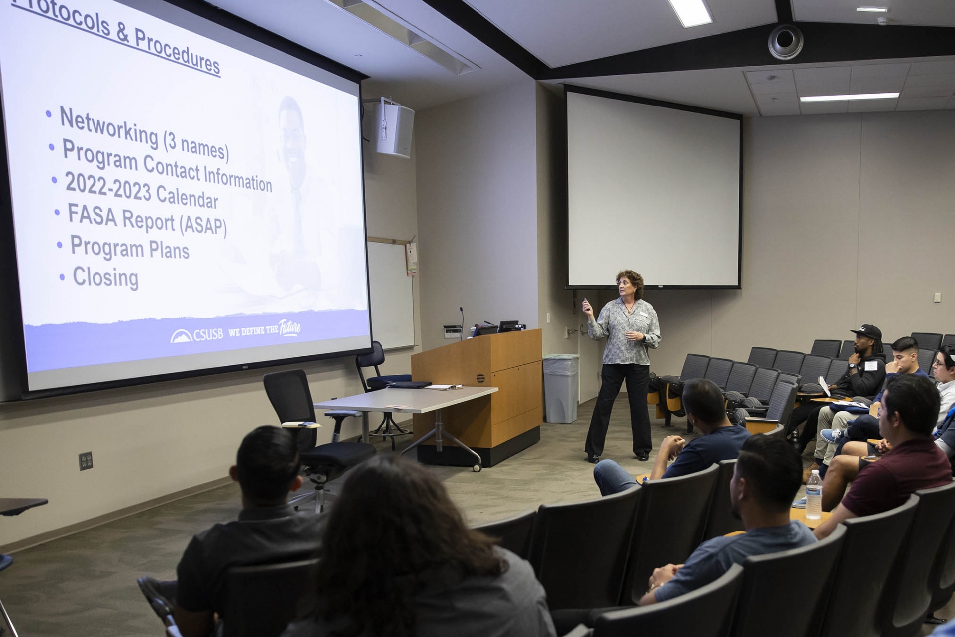 Becky Sumbera (standing), assistant dean of the Watson College of Education, speaks at a Project Impact event, May 2022. 