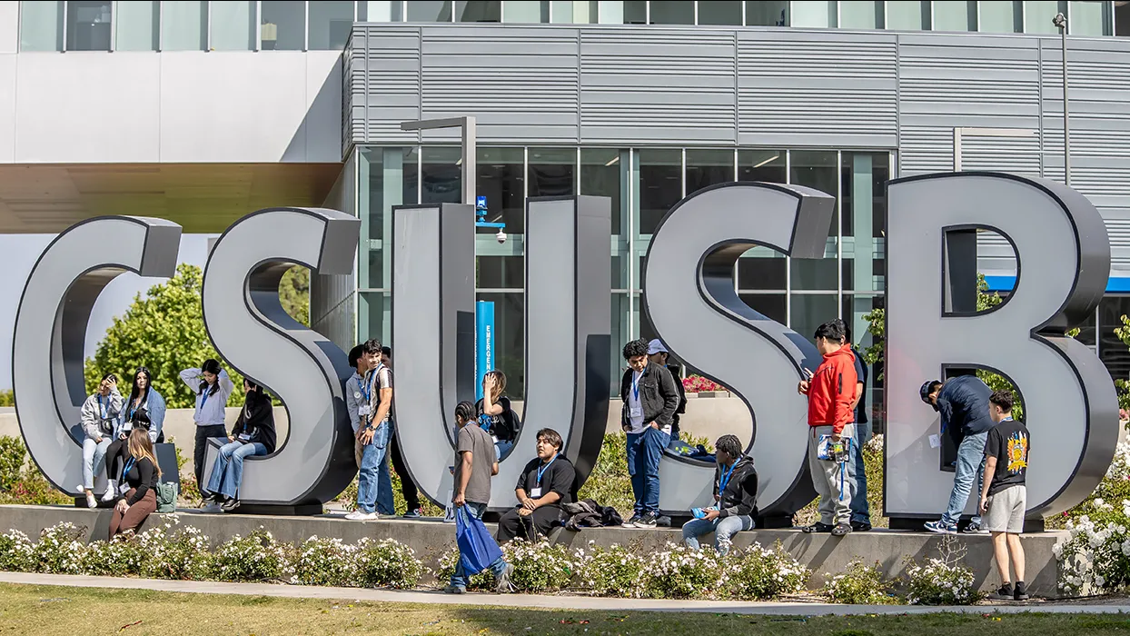 Students hanging by the CSUSB letters