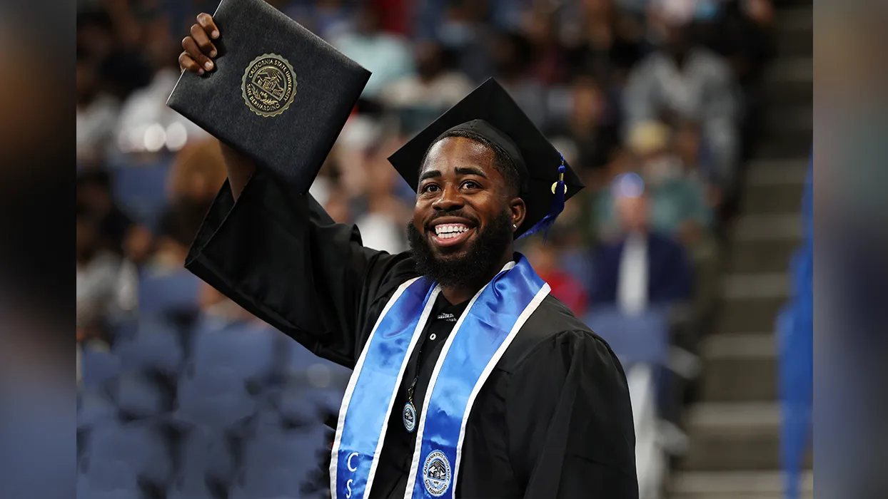 Student smiles and holds up diploma at commencement