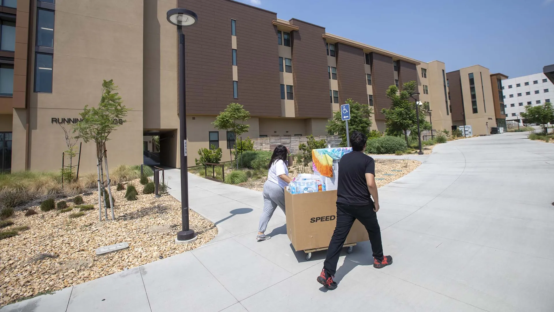 Move-in day photo of two people pushing a cart in front of a CSUSB dorm.