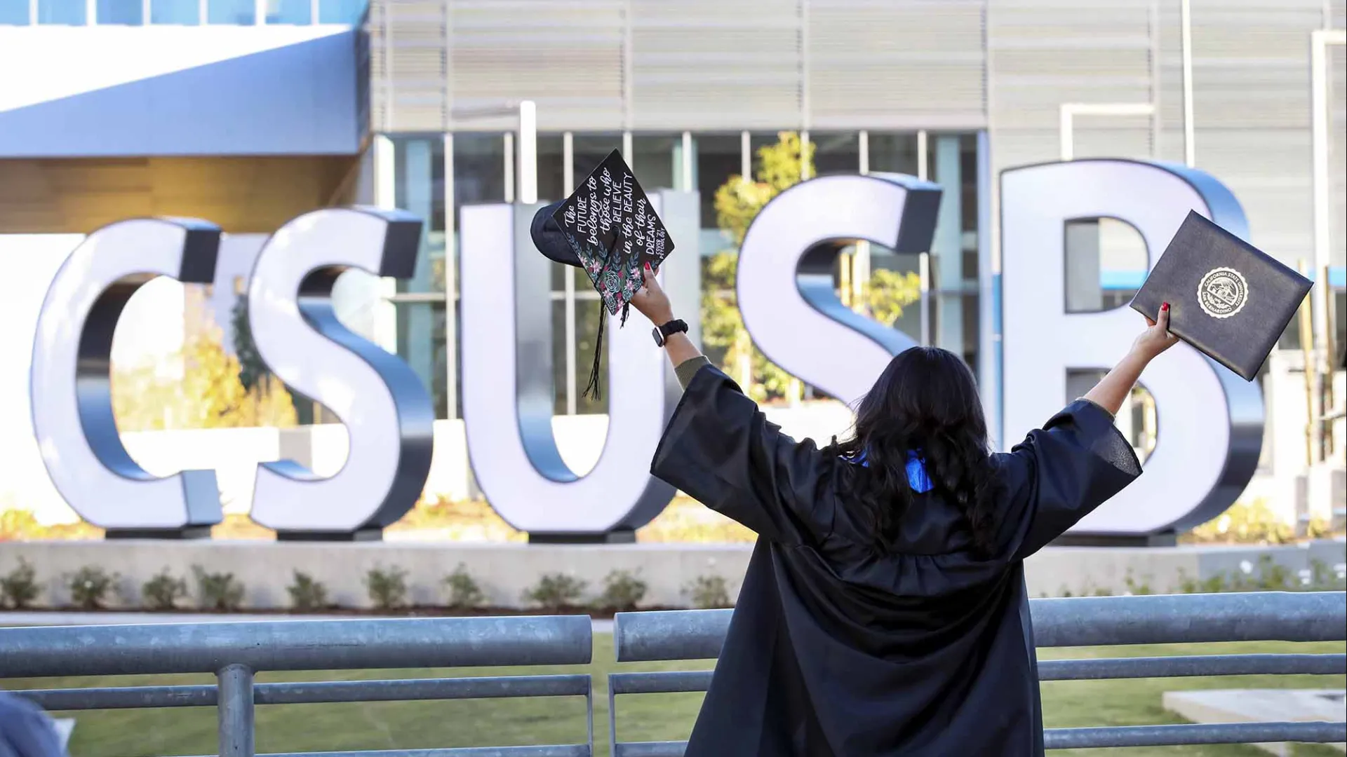 Student celebrating graduation at the CSUSB spirit letters.