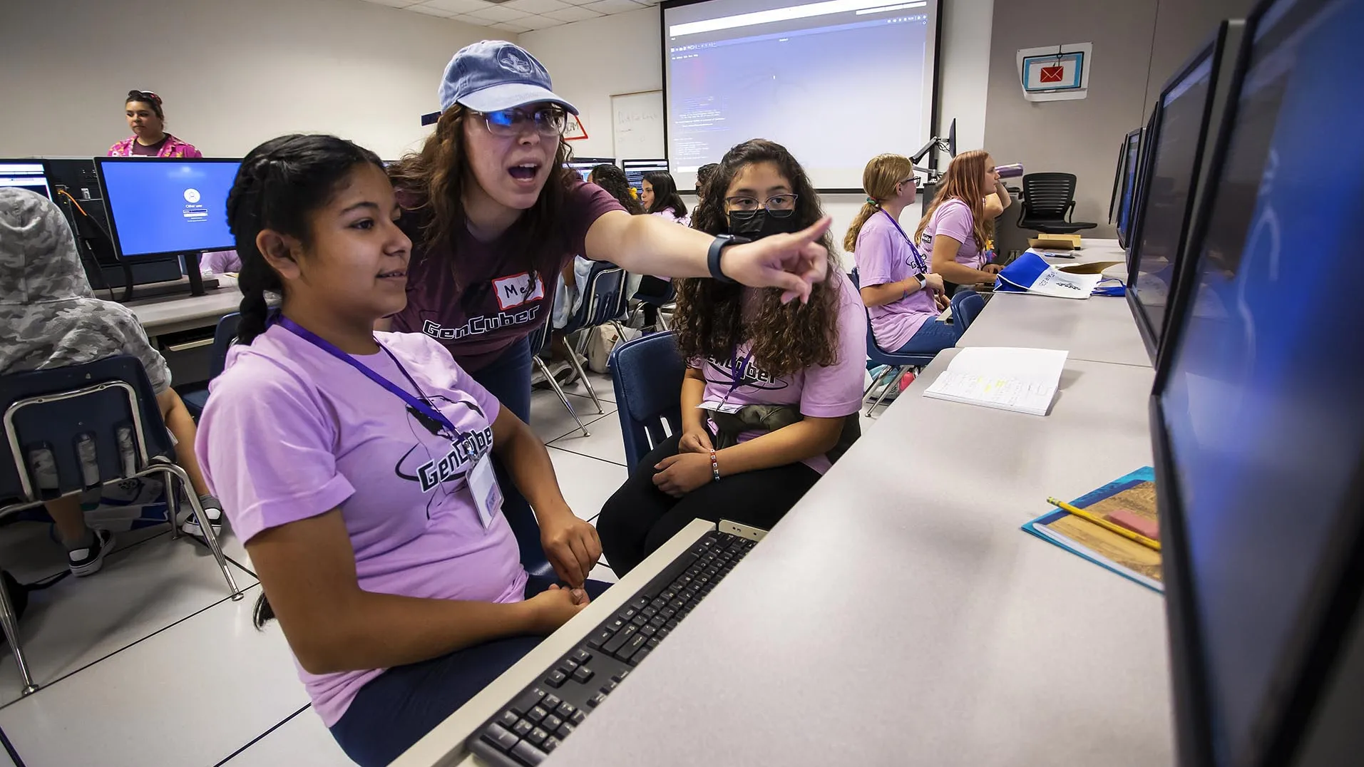 Two Girl Scouts (seated) and their cybersecurity camp instructor at a computer.