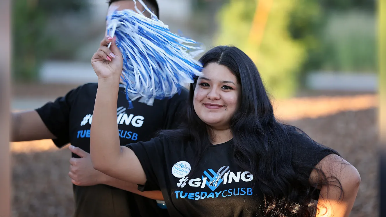 Woman wearing a Giving Tuesday T-shirt while waving a CSUSB pom pom. 