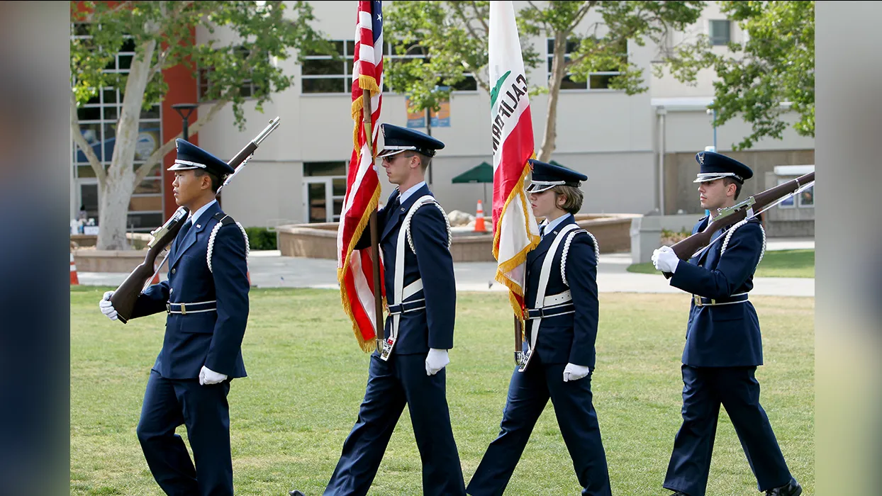 Four people in uniform march across the CSUSB lawn