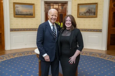 Rhian Reyes stands at right in a black dress with President Joe Biden at left, in White House, both smile widely