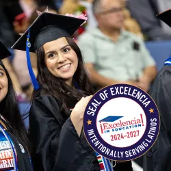 Two Cal State San Bernardino graduates at the university’s 2022 spring Commencement; the Seal of Excelencia is superimposed over the image.