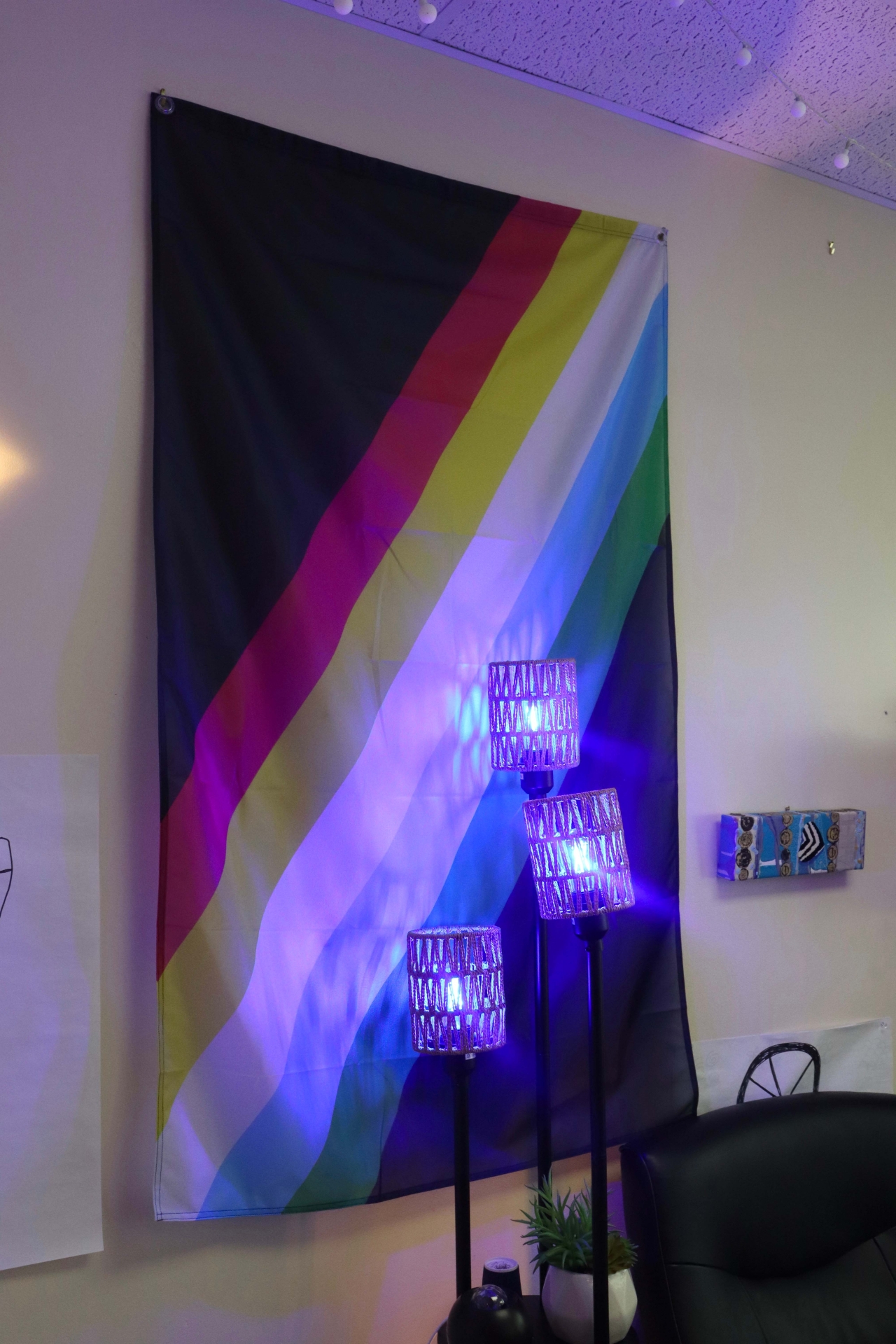 The Disability pride flag in The Cog Neurodiversity Space. Blue lights sit in front of the flag lighting a light blue ambiance in the room.