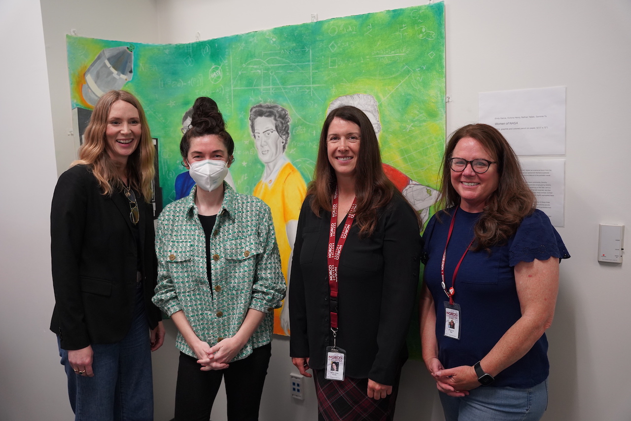 A group of four women gathers in front of a colorful painting, sharing their thoughts on the artistic display.