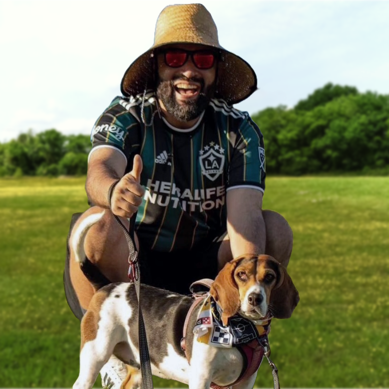 Francisco is outside by grass and large trees and smiling at the camera with his dog.