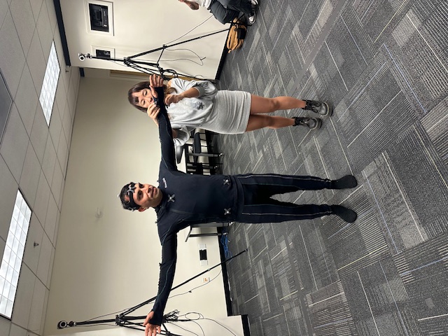 Staff memeber putting on round reflectors for a motion capture suit on a student 