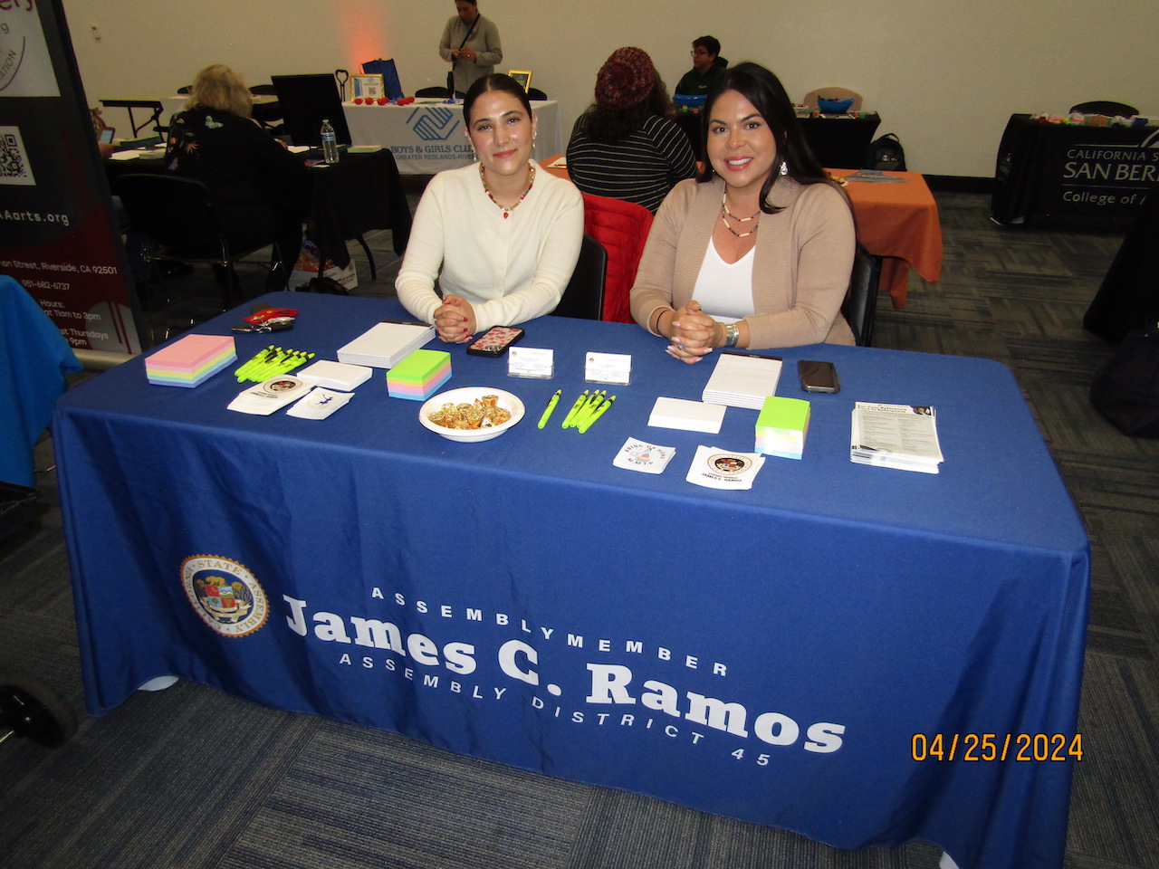 Two women sitting at a table with a sign on it.