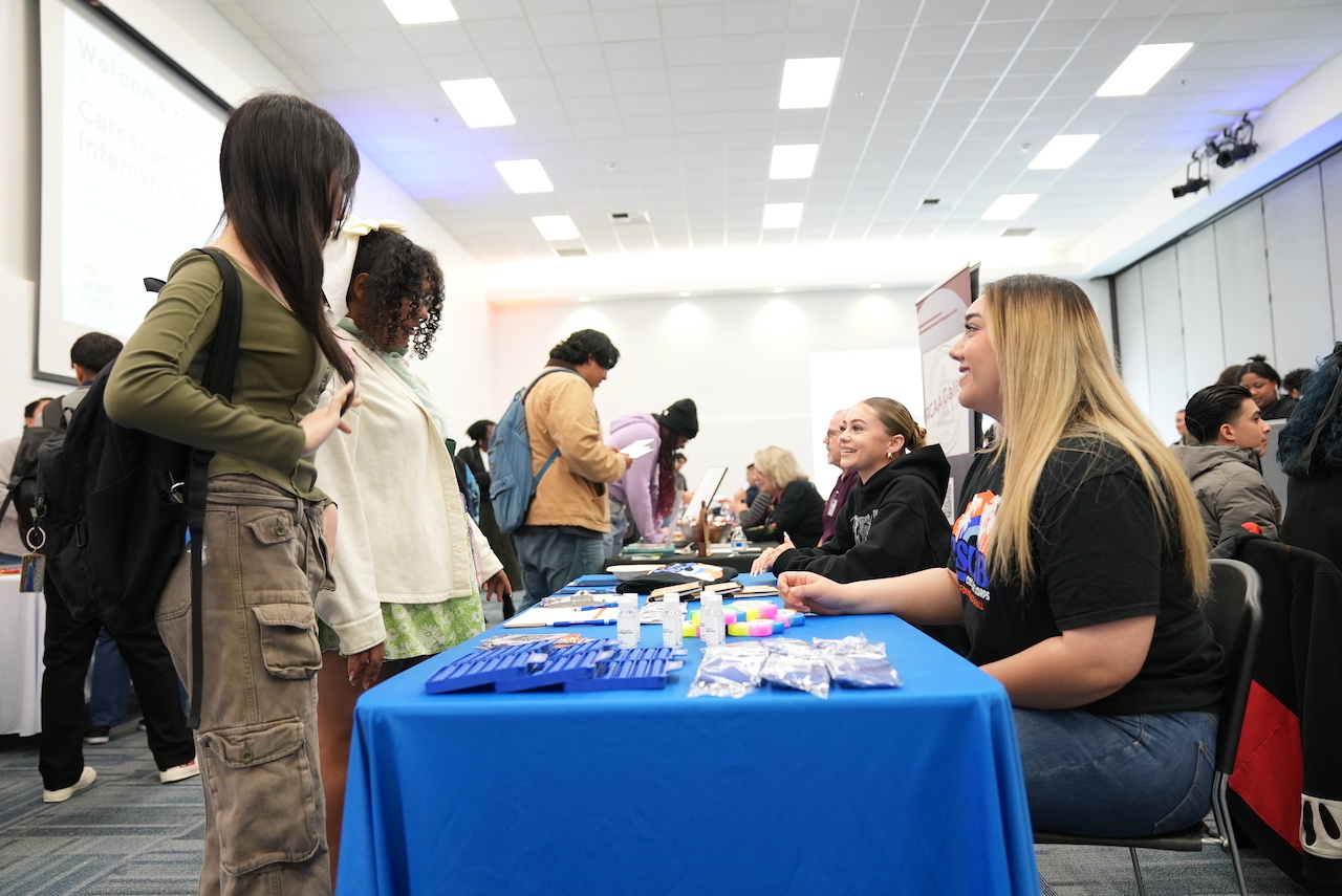 Students networking with employers at a career fair, discussing potential career paths and opportunities.