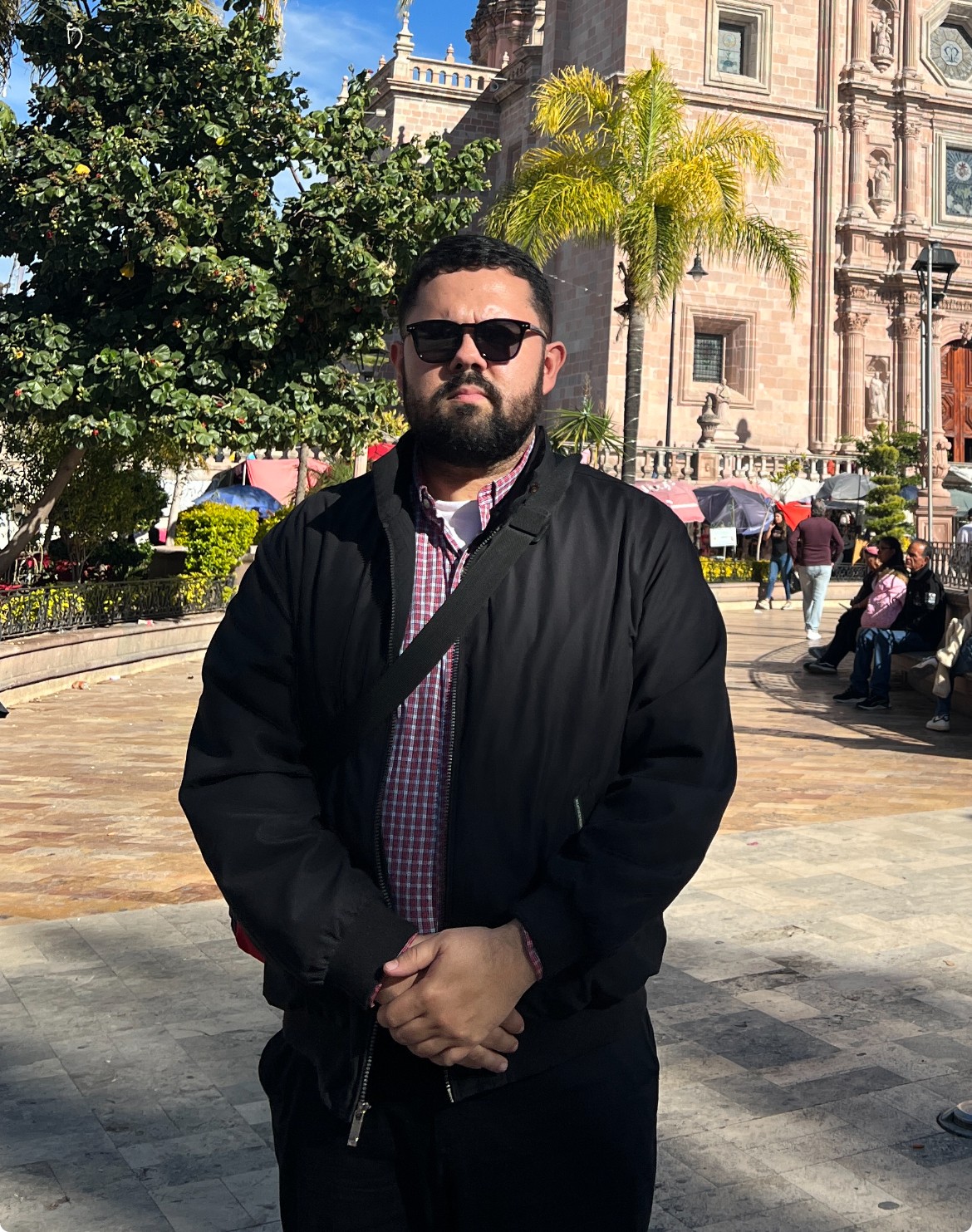 Dr. Mark A. Ocegueda, sunglasses and hands clasped, stands in front of a building facade