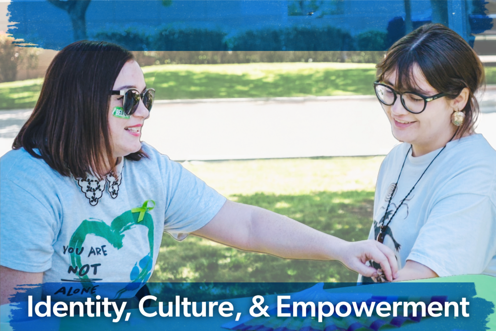 Two people outdoors share a warm interaction, smiling at each other. Both wear glasses and expressive shirts. Text reads "Identity, Culture, & Empowerment."